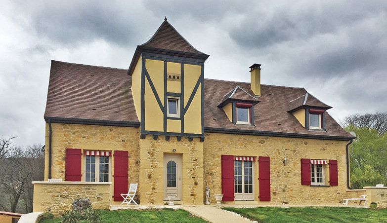 Photo de volets battants de couleur rouge installés sur les fenêtres et la porte fenêtre d'une grande maison